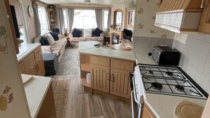 Une cuisine compacte pour camping-car, dotée d’un îlot central, d’un coin repas avec un canapé et d’un petit téléviseur.