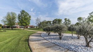 A landscaped garden with a curved pathway, trees, and a building in the background. - Romantic escape in luxury Italian villa, (Veneto)