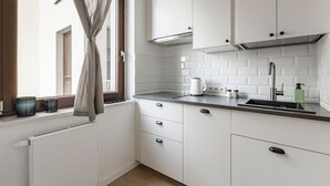 A modern kitchen with white cabinets, a black countertop, and a window with curtains. - Homewell Apartments Żelazko (Poznan)