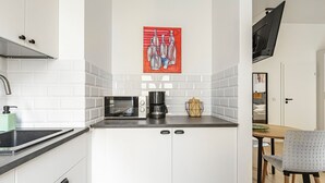 A compact kitchen with white cabinets, a microwave, a coffee maker, and a red artwork on the wall. - Homewell Apartments Żelazko (Poznan)
