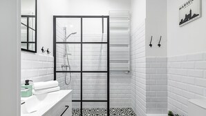 A modern bathroom with white subway tiles, a black-framed glass shower enclosure, and a tiled floor with a geometric pattern. - Homewell Apartments Żelazko (Poznan)