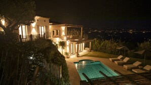 A nighttime view of a house with a swimming pool, outdoor seating, and a view of the city in the background.