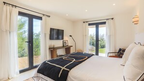A modern bedroom with a large bed, a flat-screen TV, and a balcony view.