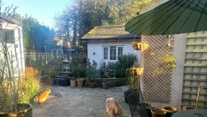 Une terrasse dallée de pierres, agrémentée de plantes en pot, un petit bâtiment blanc, ainsi qu’une table et une chaise en métal.
