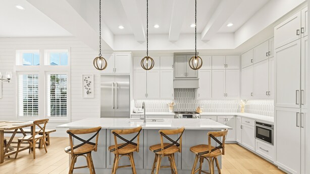A modern kitchen with white cabinetry, a central island with bar stools, and a dining area with wooden chairs. - Inviting Beach Home w/ Cinnamon Shore South Style & Amenities (Port Aransas)