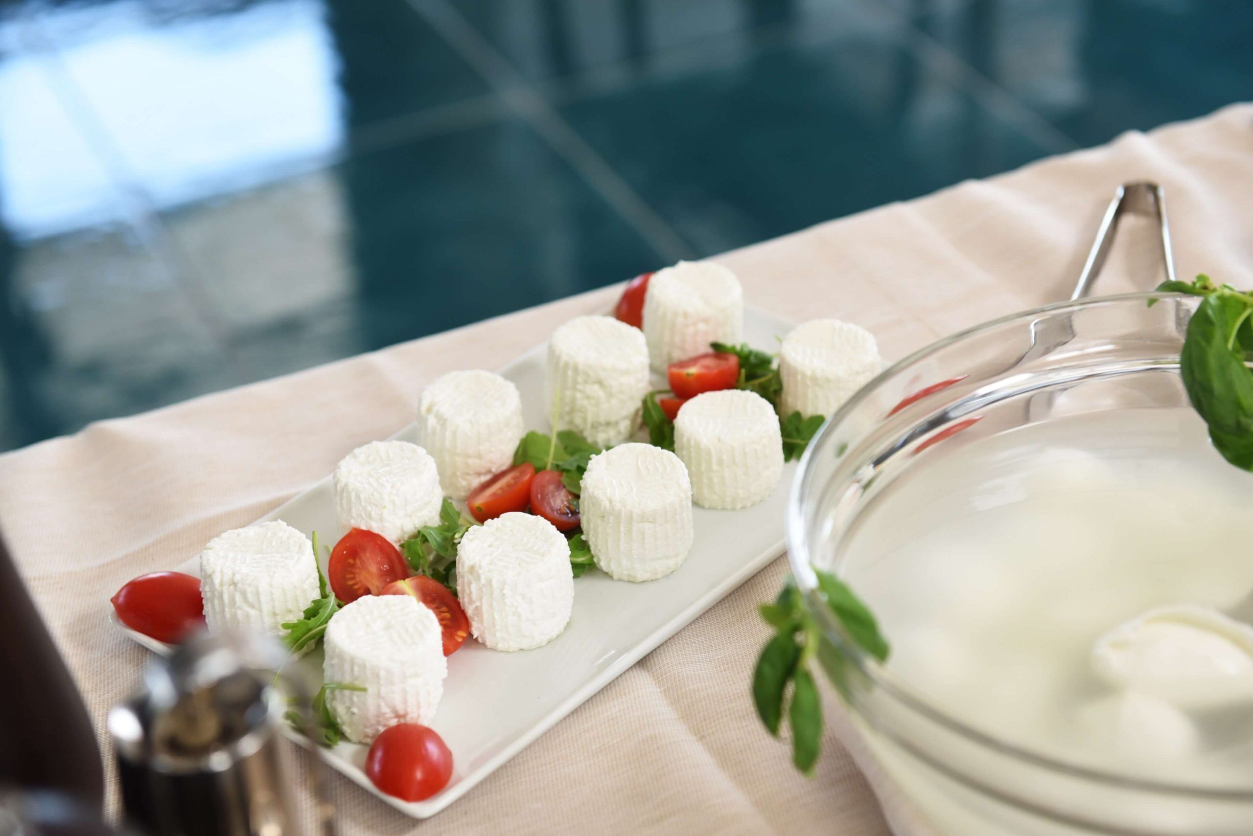 A white rectangular plate with white cheese balls and cherry tomatoes on a beige cloth.