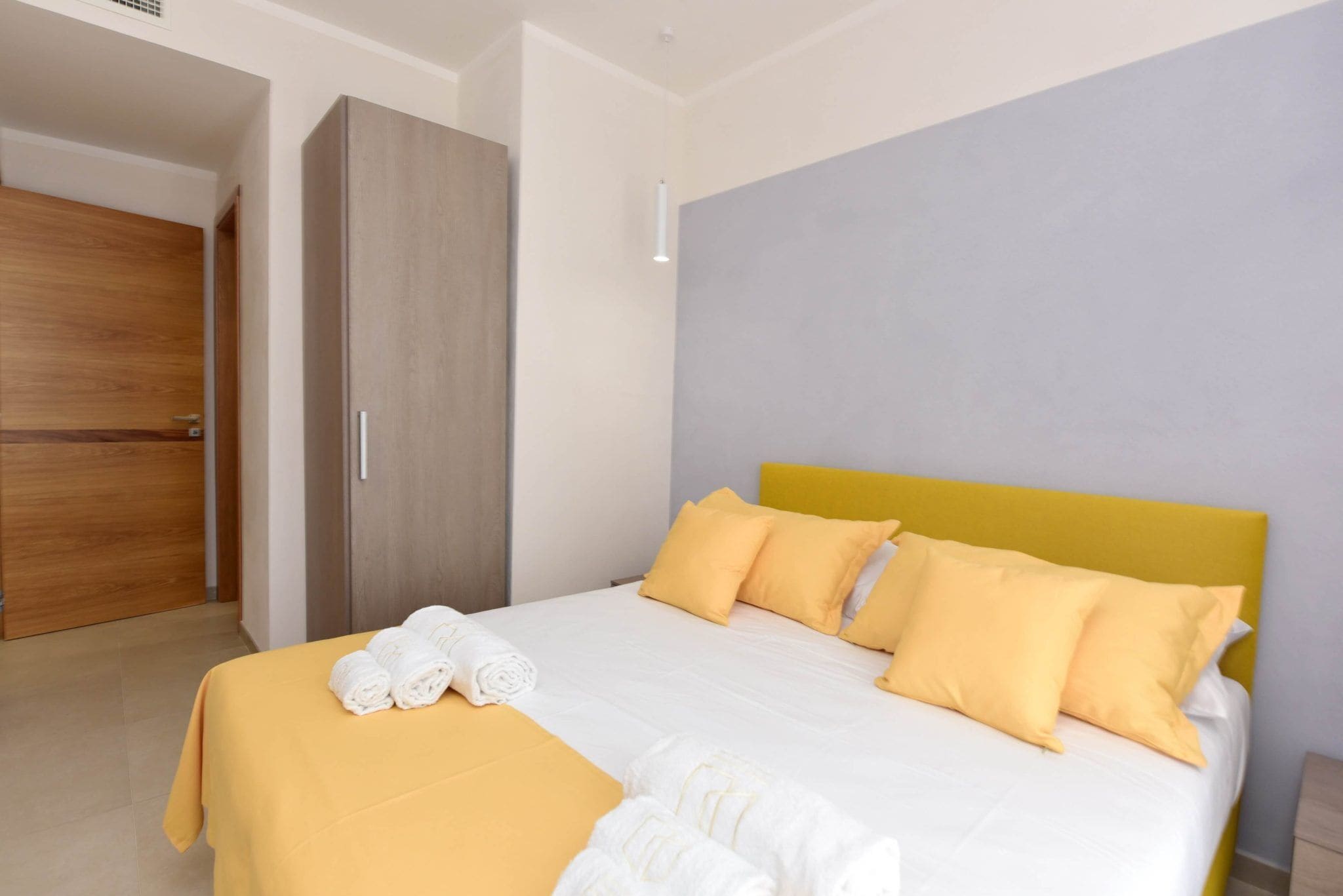 Une chambre d’hôtel avec un lit, des oreillers jaunes, une armoire en bois et une tête de lit jaune.