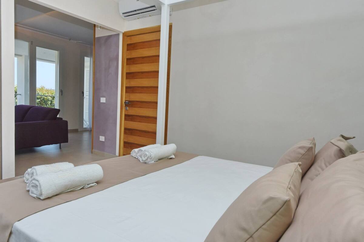 A hotel room with a bed, a wooden door, and a view of a balcony.