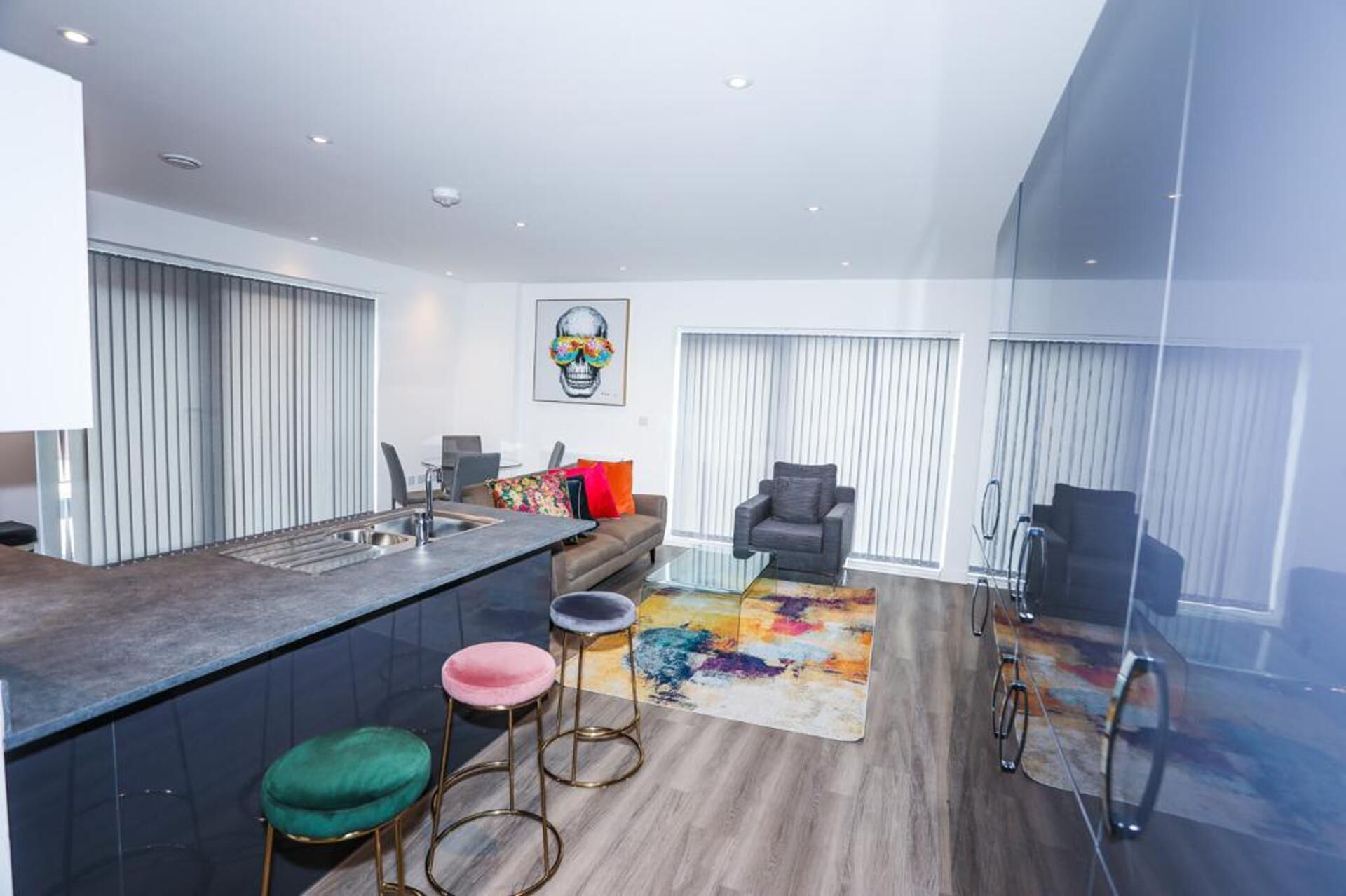 A modern kitchen with a bar area, a dining area with a sofa and chairs, and a living room with a large window and a TV.