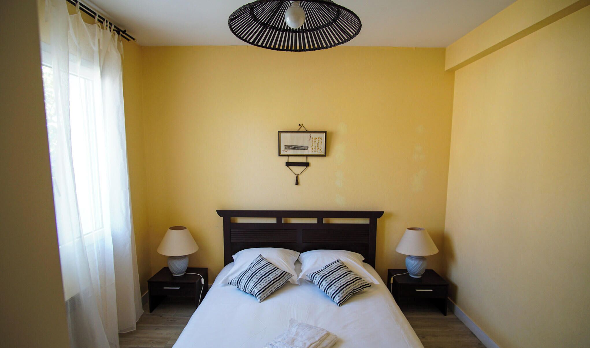 Une chambre d’hôtel comprenant un lit, deux tables de chevet avec des lampes, une œuvre d’art accrochée au mur et un ventilateur de plafond.