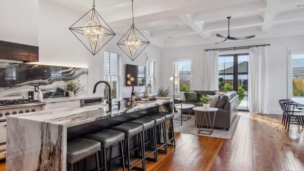 A modern kitchen with a marble island, black bar stools, and pendant lighting. - Deluxe Modern Home, Heated Pool & Game Room (New Orleans)