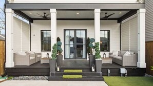 A modern house with a covered porch, two sofas, and potted plants. - Deluxe Modern Home, Heated Pool & Game Room (New Orleans)