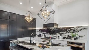 A modern kitchen with a marble countertop, black cabinets, and pendant lighting. - Deluxe Modern Home, Heated Pool & Game Room (New Orleans)