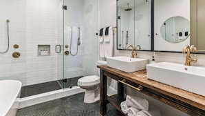 A modern bathroom with a glass-enclosed shower, a white toilet, and two sinks with gold fixtures. - LGD Designer Dream Condo | Heated Pool (New Orleans)