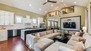 A spacious living area with a large sofa set, a dining table, and a kitchen with white cabinets. - LGD Designer Dream Condo | Heated Pool (New Orleans)