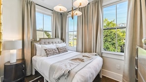 A bedroom with a large bed, a nightstand, a dresser, and a window with curtains. - LGD Designer Dream Condo | Heated Pool (New Orleans)