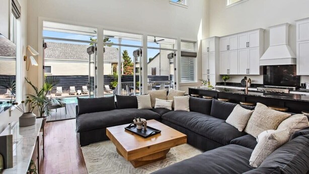 A spacious living room with a large sectional sofa, a wooden coffee table, and a view of the backyard through large sliding glass doors.
