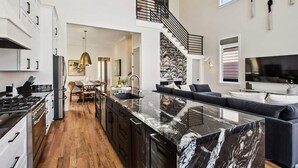 A modern kitchen with a marble island, a dining area with a chandelier, and a staircase leading to an upper level.