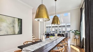 A dining area with a long wooden table, wicker chairs, and two gold pendant lights.