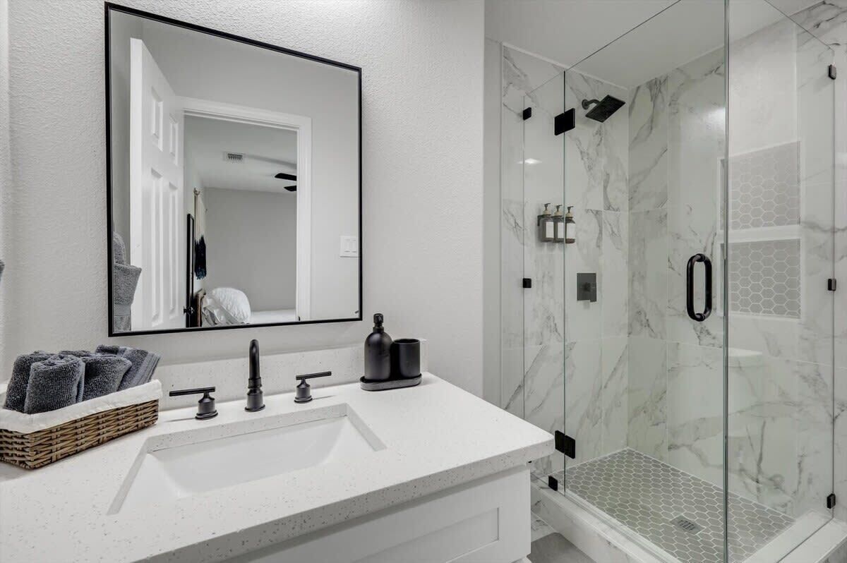 Une salle de bain moderne avec un lavabo blanc, un robinet noir et une douche séparée par des parois en verre, le tout agrémenté de murs en marbre.