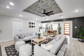 A modern living room with a sofa, coffee table, and chairs. There is a kitchen in the background with a dining area.