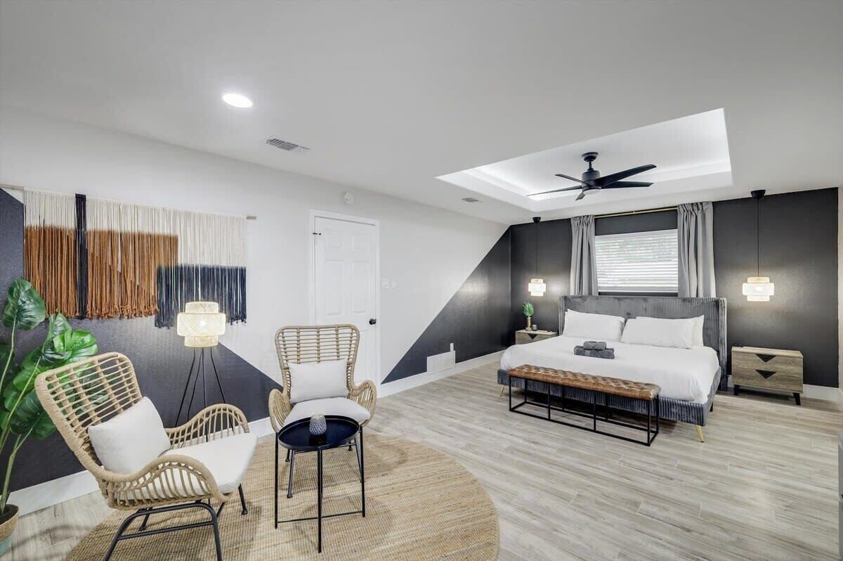 A modern bedroom with a bed, two chairs, a small table, a ceiling fan, and a skylight.