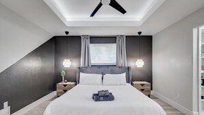 A modern bedroom with a large bed, two bedside tables, a ceiling fan, and a window with curtains.