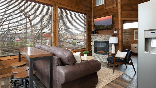 A cozy living room with a leather sofa, a stone fireplace, and a large window with blinds. - Walk2DowntownPF/GasFirepit/Waterfront (Pigeon Forge)