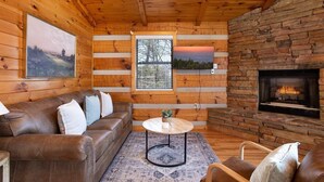 A cozy cabin interior with a wooden ceiling, a stone fireplace, a leather sofa, and a round coffee table. - Big Mt. LeConte Views/Gatlinburg (Gatlinburg)