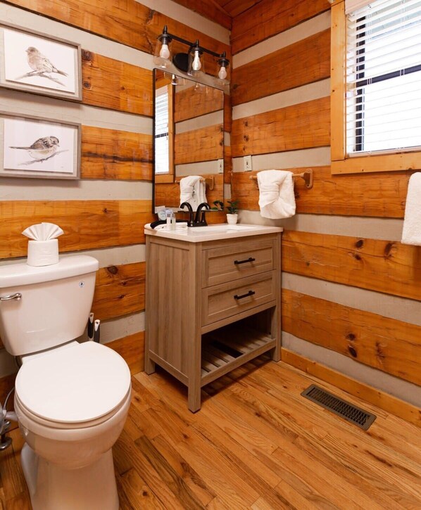 A wooden-paneled bathroom with a toilet, sink, and mirror. - Big Mt. LeConte Views/Gatlinburg (Gatlinburg)