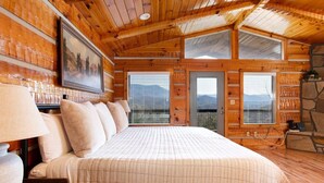A cozy wooden cabin bedroom with a large bed, a nightstand, a lamp, and a painting on the wall. - Amazing Mt. LeConte Views/Gatlinburg (Gatlinburg)