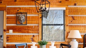 A wooden cabin interior with a round dining table, four chairs, a hanging light fixture, a window with blinds, and a door with a lock. - Amazing Mt. LeConte Views/Gatlinburg (Gatlinburg)