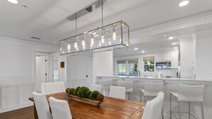 A modern kitchen with white cabinetry, a wooden dining table, and a hanging light fixture.