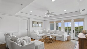 A spacious living room with a white sofa set, a coffee table, and a ceiling fan.