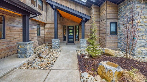 A modern log cabin with a stone facade, a covered entryway, and a landscaped front yard.