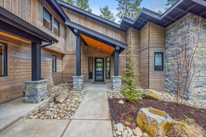 A modern log cabin with a stone facade, a covered entryway, and a landscaped front yard.