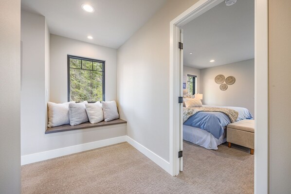 A bedroom with a built-in bench under a window, a bed with a blue bedspread, and a bedside table with a lamp.