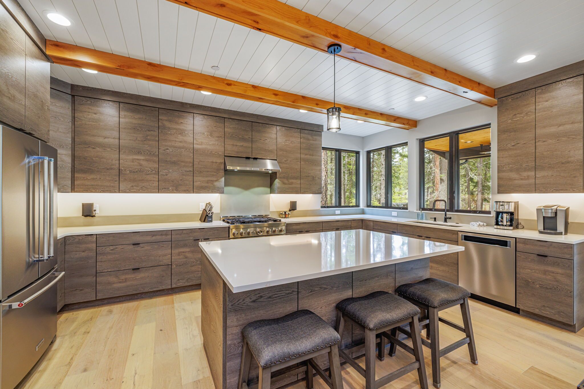 A modern kitchen with a large island, wooden cabinets, and a stainless steel refrigerator.