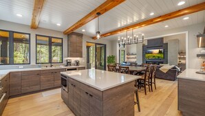 A spacious kitchen with a large island, wooden beams, and a dining area with a view of the outdoors.