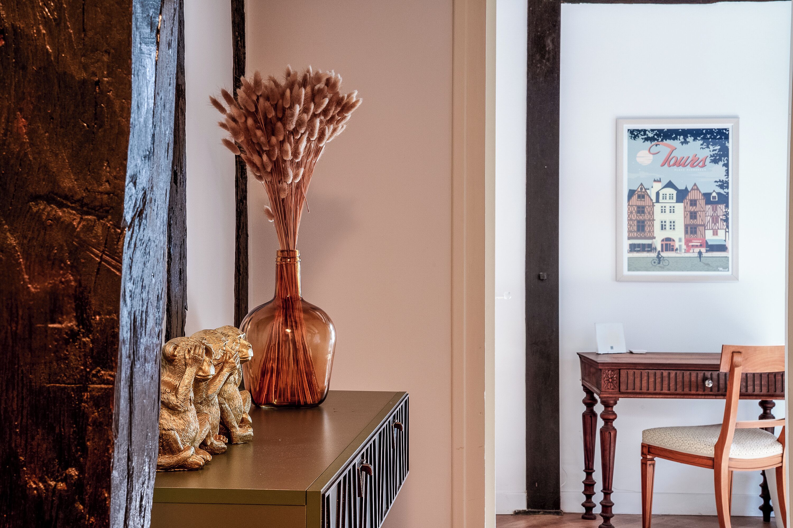 A wooden cabinet with a vase and two decorative figures, a framed picture on the wall, and a wooden chair.