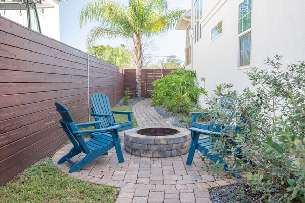 A patio with a fire pit, blue Adirondack chairs, and a wooden fence.