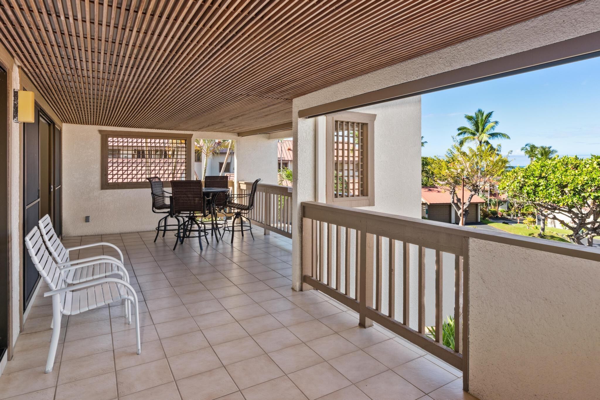 A covered outdoor area with a table and chairs, a wooden ceiling, and a view of the ocean.