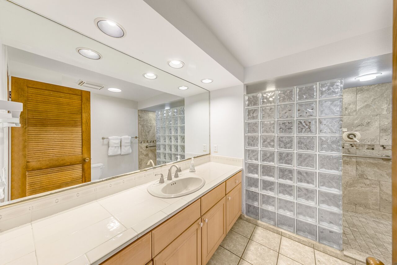 A modern bathroom with a large mirror, two sinks, wooden cabinets, and a glass shower enclosure.