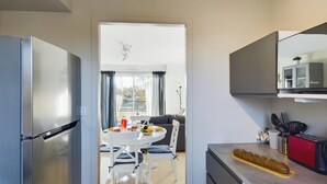 A modern kitchen with a refrigerator, a dining table with chairs, a kitchen island, and a large window. - -LITTO- CONCARNEAU AVEC TERRASSE PROCHE COMMERCES (Concarneau)