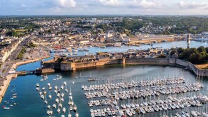 A harbor with numerous boats docked, a fortified structure, and a cityscape in the background. - -LITTO- CONCARNEAU AVEC TERRASSE PROCHE COMMERCES (Concarneau)