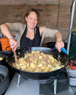 A person cooking in a large wok with potatoes and meat.