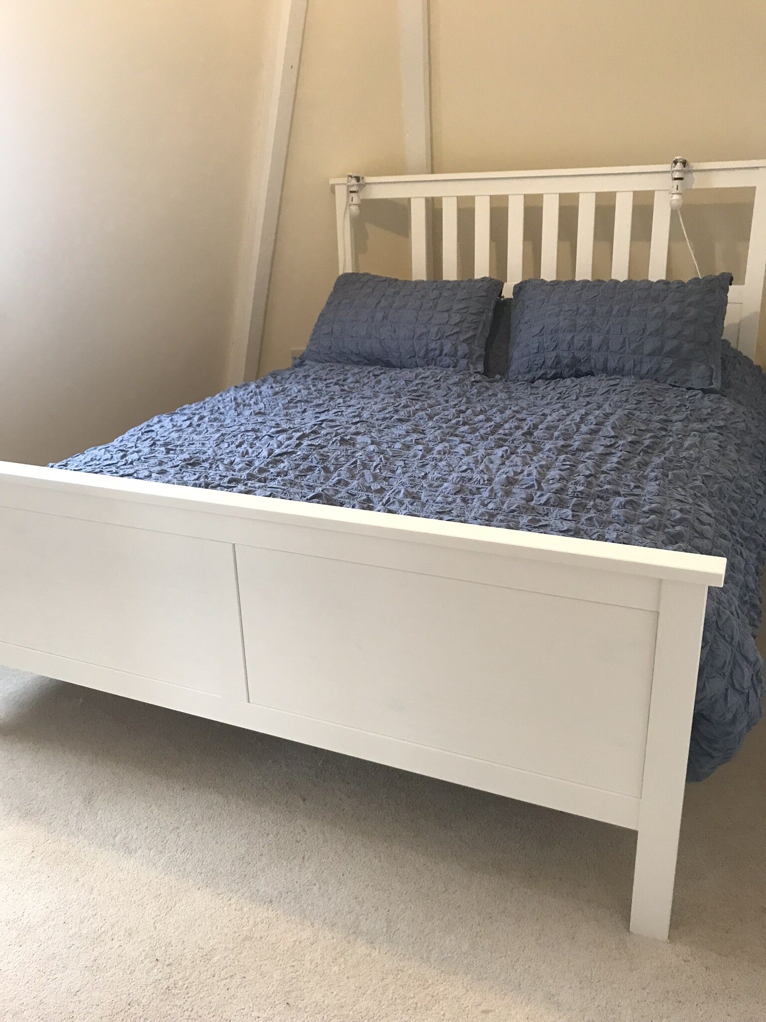 En seng med hvidt stel og et blåt tæppe med struktur.