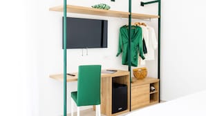 A modern room with a wooden desk, a green chair, a TV mounted on the wall, and a clothing rack with a green garment. - Vittoria Rooms Sorrento (Sorrento)