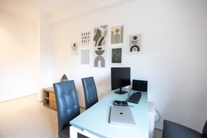 A modern office space with a desk, two chairs, a laptop, a monitor, and a keyboard. There are abstract wall art pieces and a small wooden shelf. - Vittoria Rooms Sorrento (Sorrento)