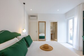 A modern hotel room with a large bed, green bedding, a straw hat on the bed, a bedside lamp, and a view of the city through large windows. - Vittoria Rooms Sorrento (Sorrento)
